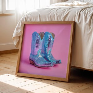 May include: A pair of blue cowboy boots with a mirrored finish, set against a pink background.