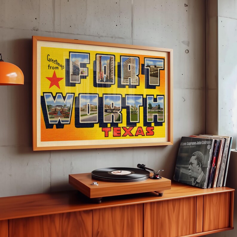 May include: A framed vintage postcard featuring a photo montage of Fort Worth, Texas. The postcard is in a wooden frame and is hanging on a grey wall. The postcard reads "Greetings from Fort Worth Texas".