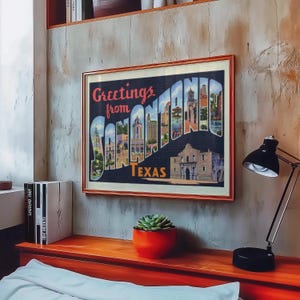 May include: Framed vintage postcard art with the text "Greetings from SAN ANTONIO TEXAS." The artwork features a collage of San Antonio landmarks and buildings. The frame is a warm brown color, and the artwork is displayed on a textured wall.