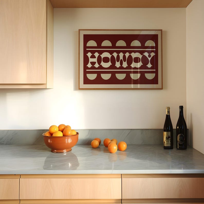 May include: A kitchen counter with a bowl of oranges, two bottles of wine, and a framed print with the word "HOWDY" in a red and white geometric design.