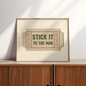 May include: A framed print of a vintage ticket with the text "STICK IT TO THE MAN" and the number "0013472" on each side.
