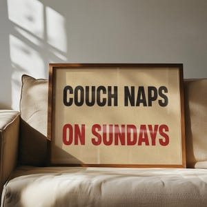 May include: A framed print with the text "Couch Naps on Sundays" in black and red lettering on a beige background.