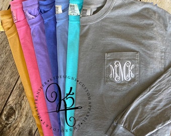 May include: A variety of long-sleeve t-shirts in different colors, including mustard yellow, pink, purple, blue, and turquoise. The shirts have a pocket on the left side with a white embroidered monogram "MCK". The shirts are made by K5Designs.