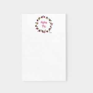 May include: White notepad with a floral wreath design and the text "Alpha Phi" in pink lettering.