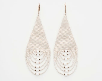 May include: A pair of long, white beaded earrings with a teardrop shape. The earrings have multiple rows of beads and are accented with small, white beads.