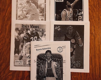 May include: A collection of vintage sports trading cards featuring black and white images of athletes. The cards include baseball, basketball, and football players. The cards are arranged on a wooden surface.