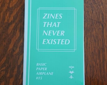 May include: A teal blue booklet with the title "Zines That Never Existed" and the text "Basic Paper Airplane #15".
