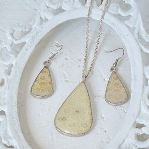 May include: A set of jewelry featuring a teardrop-shaped pendant and matching earrings. The pendant and earrings are made of a light beige material with a textured surface, resembling fossilized coral. The jewelry is set in silver.