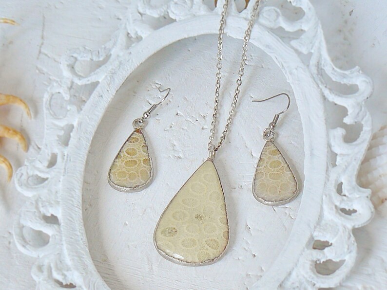 May include: A set of jewelry featuring a teardrop-shaped pendant and matching earrings. The pendant and earrings are made of a light beige material with a textured surface, resembling fossilized coral. The jewelry is set in silver.