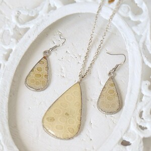 May include: A set of teardrop-shaped earrings and a necklace with a light beige pendant. The pendant and earrings feature a unique pattern of small circles.