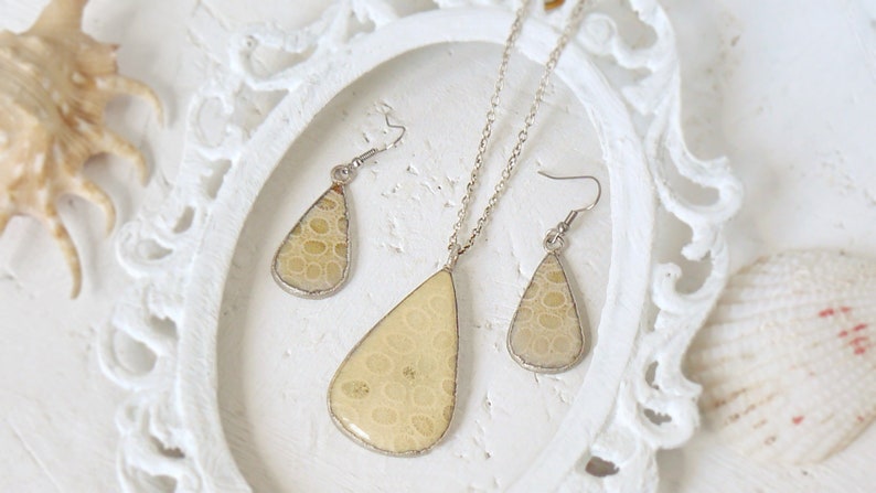 May include: A set of teardrop-shaped earrings and a necklace with a light beige pendant. The pendant and earrings feature a unique pattern of small circles.