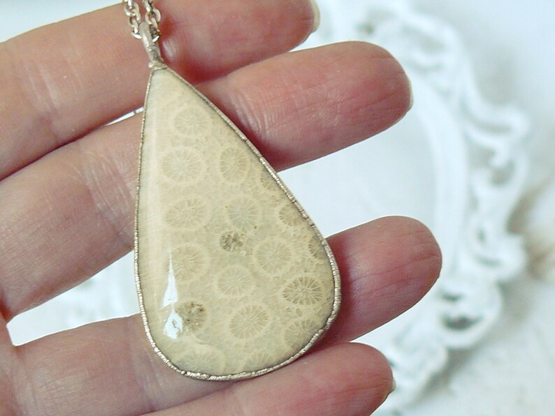 May include: A teardrop-shaped pendant necklace with a white fossilized coral stone set in silver.