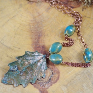 Puede incluir: Un collar de cadena de cobre con cuentas de cerámica turquesa y verde y un gran colgante de hoja de color cobre.