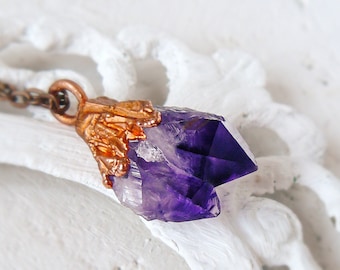 May include: A purple amethyst crystal pendant with a copper setting. The pendant is attached to a copper chain.