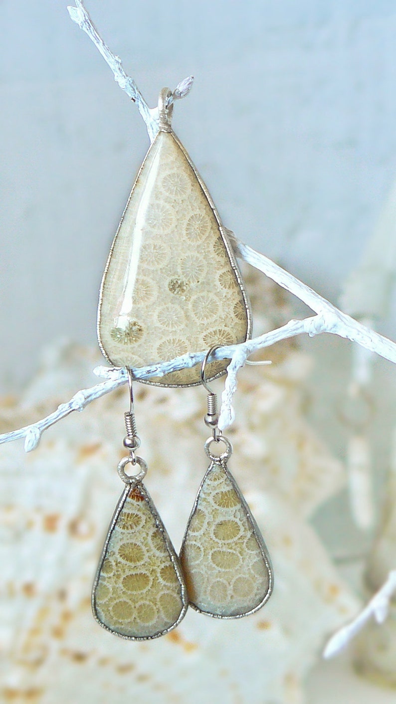 May include: A set of silver earrings and a pendant featuring fossilized coral in a teardrop shape. The coral is a light beige color with a swirling pattern.