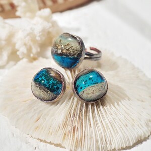 May include: A set of three rings with blue and white glass inlays. The rings are made of copper and have a rustic finish.