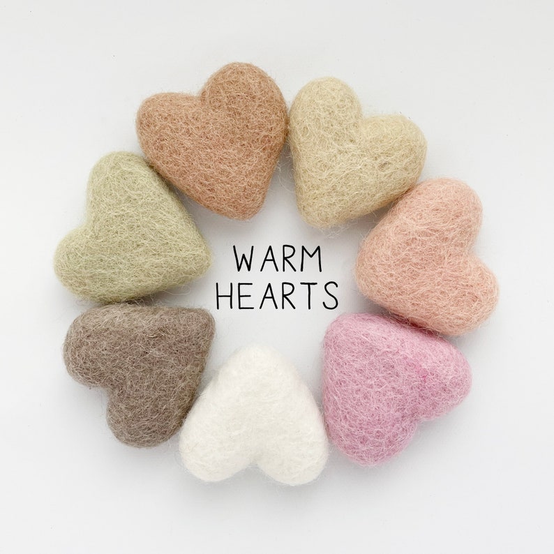 May include: A collection of eight heart-shaped felt ornaments in various neutral colors, arranged in a circle. The colors include shades of beige, pink, brown, and white. The text "WARM HEARTS" is displayed in black, centered below the hearts.