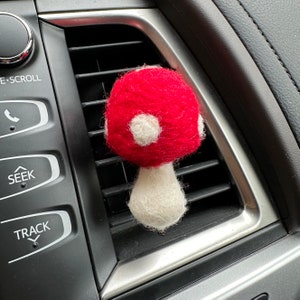 May include: A red and white felt mushroom car air freshener hanging from a car's air vent.