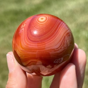 May include: A red carnelian sphere with white banding. The sphere is smooth and polished, and the banding is visible throughout the stone.