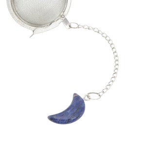 May include: A silver tea infuser with a mesh ball and a chain attached to a blue crescent moon-shaped charm.