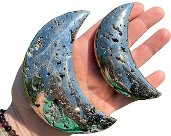 May include: Two crescent moon shaped pyrite crystals. The larger crystal is about 5 inches long and the smaller crystal is about 3 inches long. Both crystals have a metallic silver color with a rough, textured surface.