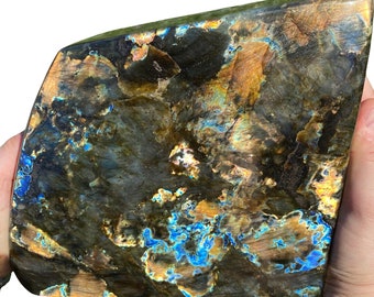 May include: A large, irregularly shaped piece of labradorite with a dark gray, brown, and blue iridescent sheen. The stone has a rough, natural surface.