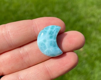 Puede incluir: Un cabujón en forma de media luna de color azul y verde, también conocido como aragonito, se sostiene en una mano.