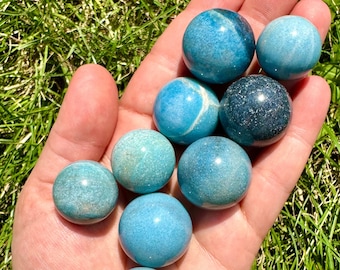 May include: A collection of eight smooth, polished blue and green gemstone spheres. The spheres are various shades of blue and green, with some having a sparkly, iridescent finish.