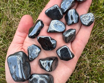 Puede incluir: Una colección de piedras de hematites pulidas, lisas y negras. Las piedras son de varios tamaños y formas, con un acabado brillante y metálico.