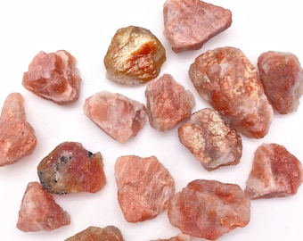 May include: A collection of 13 sunstone crystals in various sizes and shapes. The crystals are a mix of orange, red, and gold colors with a translucent appearance.