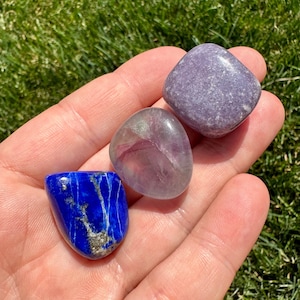 May include: Three tumbled stones, a purple fluorite, a blue lapis lazuli, and a lavender lepidolite.