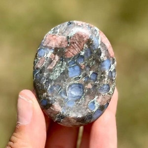 Könnte beinhalten: Ein glatter, ovaler polierter Stein mit einem einzigartigen Muster aus Blau, Grün und Rosa. Der Stein hat eine gesprenkelte Optik mit einer Vielzahl von Farben und Texturen.