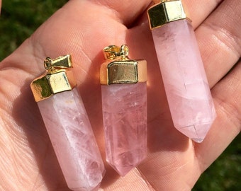 May include: Three pink rose quartz crystal pendants with gold-toned metal caps. The pendants are in the shape of a point and are approximately 2 inches long.