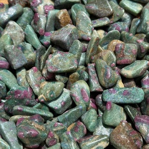 May include: A collection of green and pink ruby zoisite tumbled stones. The stones are smooth and polished, with a variety of shapes and sizes.