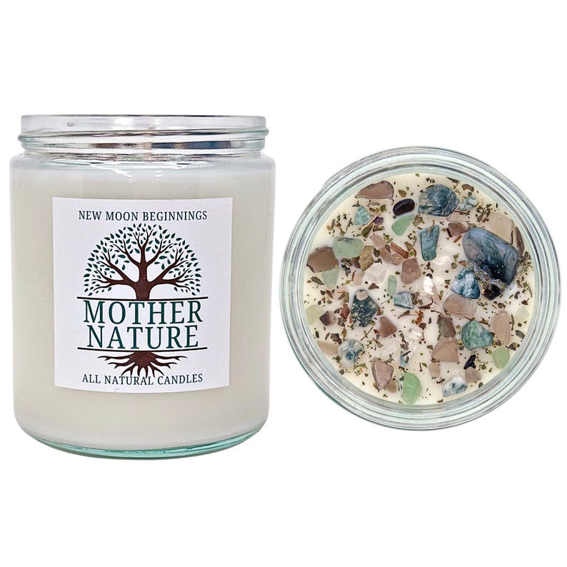 May include: A white candle with a clear glass jar and a label that reads "New Moon Beginnings Mother Nature All Natural Candles". The candle is decorated with small pieces of green, brown, and white stones.