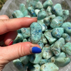 May include: A bowl filled with tumbled blue green azurite stones. The stones are smooth and have a variety of shapes and sizes.