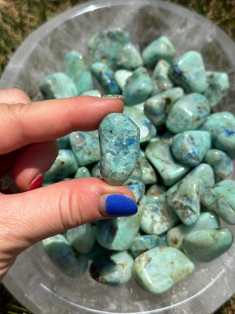 May include: A bowl filled with tumbled blue green azurite stones. The stones are smooth and have a variety of shapes and sizes.
