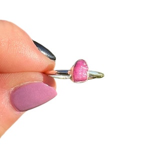 May include: A silver ring with a pink, raw gemstone set in the band.