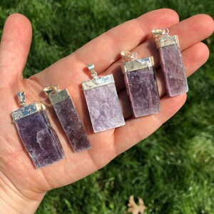 May include: Six silver pendant charms with purple lepidolite crystal stones. The stones are rectangular and have a natural, raw look. The pendants are ready to be added to a necklace or bracelet.