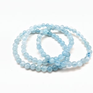 May include: Three light blue aquamarine beaded bracelets stacked together. The beads are round and smooth.