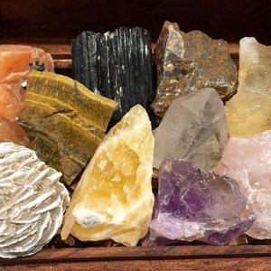 May include: A wooden box filled with a variety of crystals, including clear quartz, amethyst, rose quartz, tiger's eye, calcite, and selenite.