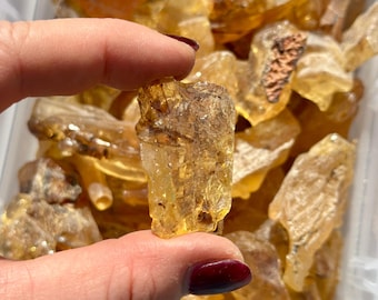 Könnte beinhalten: Eine Sammlung von rohen, durchscheinenden Bernsteinsteinen in goldgelben und honigorangen Farbtönen. Die Stücke haben unregelmäßige, gezackte Formen mit natürlichen Texturen und sichtbaren Einschlüssen, die ein glänzendes Aussehen haben.