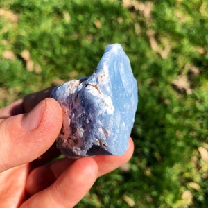 May include: A light blue, rough-textured, natural stone with white and brown markings. The stone is being held in a hand.