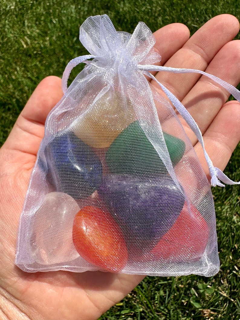 May include: A white organza bag filled with seven tumbled chakra stones. The stones are clear, yellow, green, blue, purple, red, and orange.