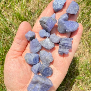 May include: A collection of blue kyanite crystals, some with a more purple hue, in various shapes and sizes. The crystals are rough and unpolished, with a natural, earthy appearance.