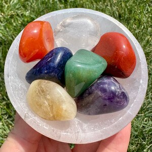 May include: Seven chakra stones in a white selenite bowl. The stones are red, orange, yellow, green, blue, indigo, and violet.