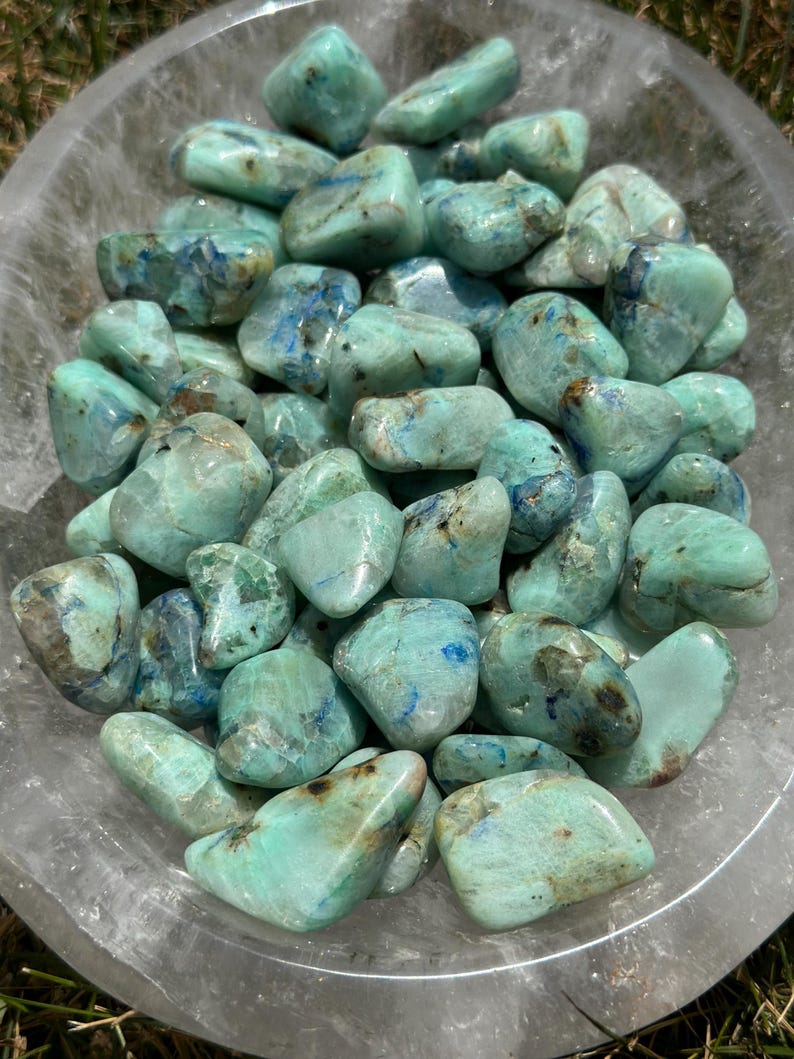 May include: A bowl of tumbled green and blue chrysocolla stones. The stones are smooth and polished, with a variety of shapes and sizes.