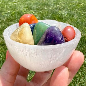 May include: A white selenite bowl filled with seven chakra stones. The stones are red, orange, yellow, green, blue, indigo, and violet.