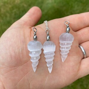K&ouml;nnte beinhalten: Drei Selenit-Kristall-Anh&auml;nger in Spiralform mit silberfarbenen Metallscharnieren. Die Anh&auml;nger sind in verschiedenen Gr&ouml;&szlig;en, der gr&ouml;&szlig;te ist etwa 5 cm lang.
