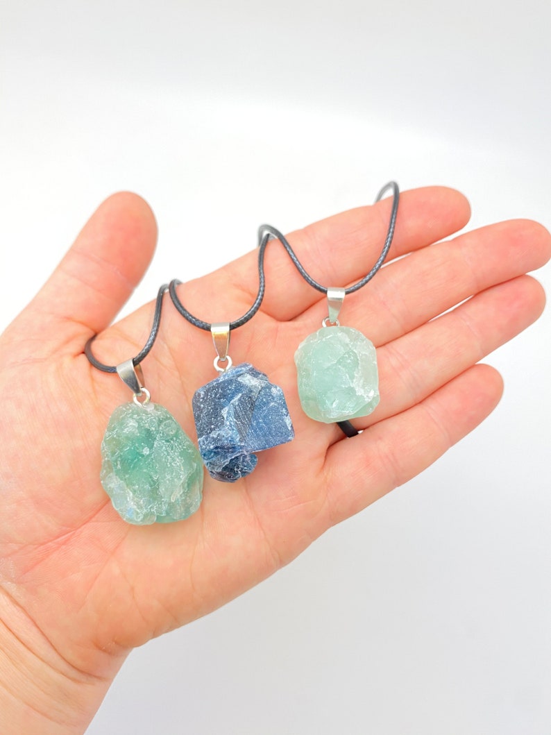 Puede incluir: Tres collares de cristal en bruto en cordones negros. Los cristales son verde claro, verde oscuro y azul gris&aacute;ceo.